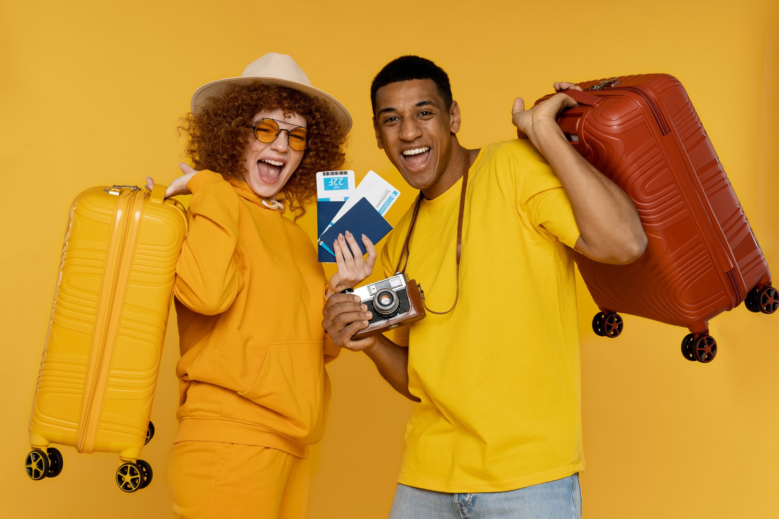 Two people in yellow outfits holding suitcases and travel documents, smiling