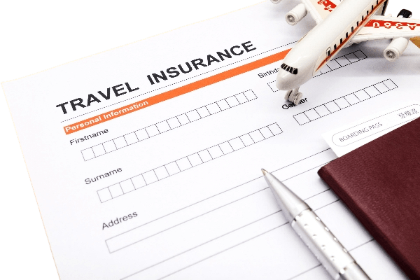 Travel insurance form partially filled out with sections for personal information, accompanied by a silver pen, maroon passport, boarding pass, and model airplane, symbolizing preparation for a trip and securing coverage